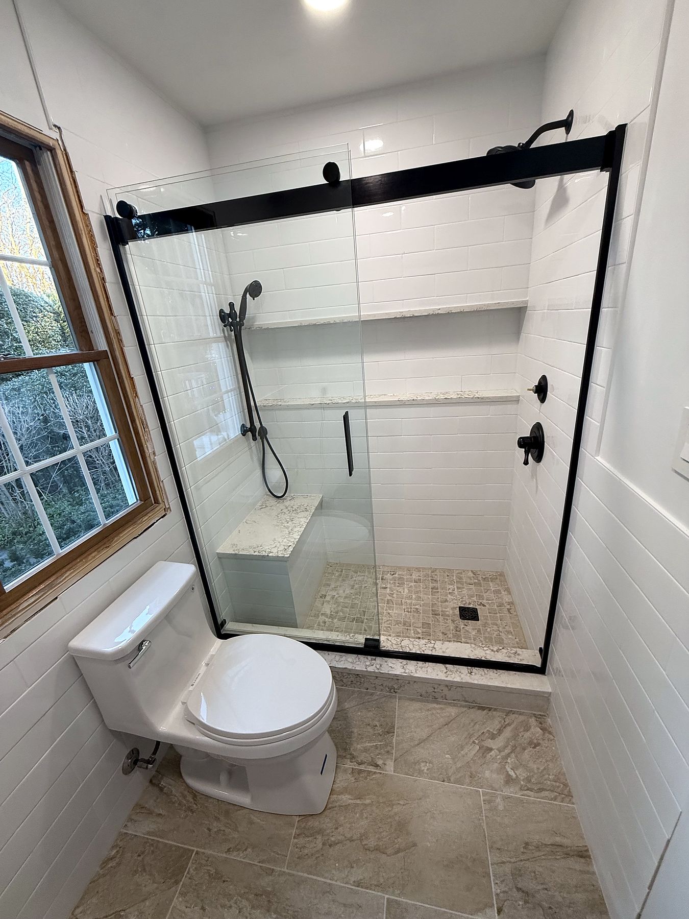 Walk-in shower with white tile, matte black fixtures and built-in bench