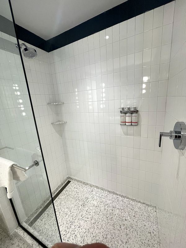 White tile walk-in shower with pebble floor and glass panel
