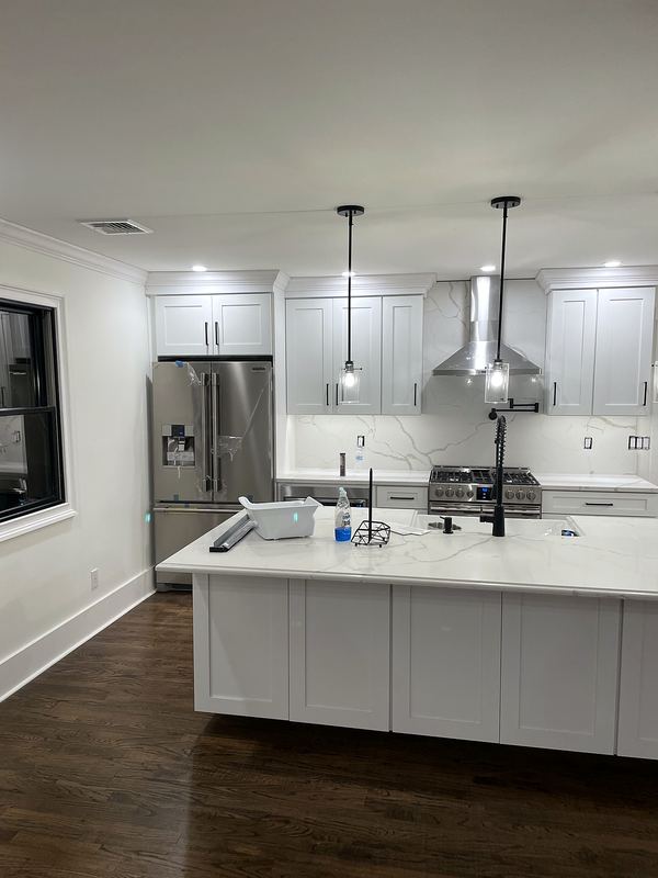 White kitchen with large island, pendant lights and stainless hood