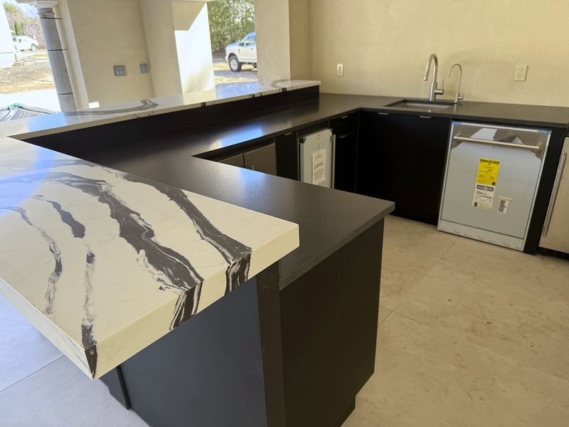 Outdoor kitchen with black cabinets and a waterfall countertop with bold black veining