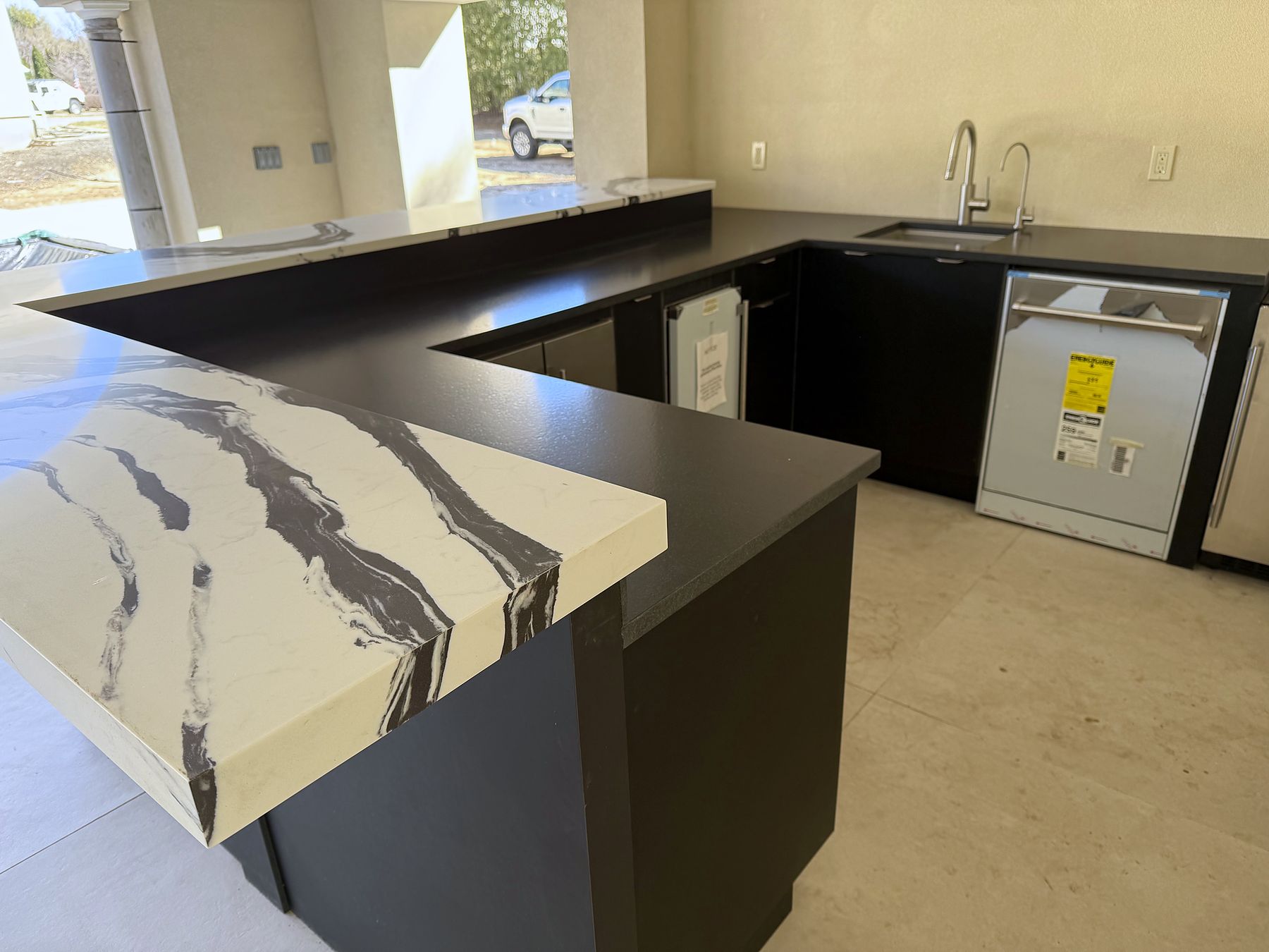 Outdoor kitchen with black cabinets and a waterfall countertop with bold black veining