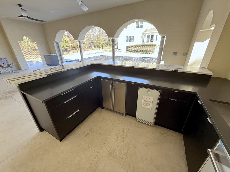 L-shaped outdoor kitchen with black cabinets, sink and dishwasher